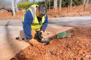 Worker installing a drainage pipe to fix water runoff issues near a concrete driveway in North Royalton OH.